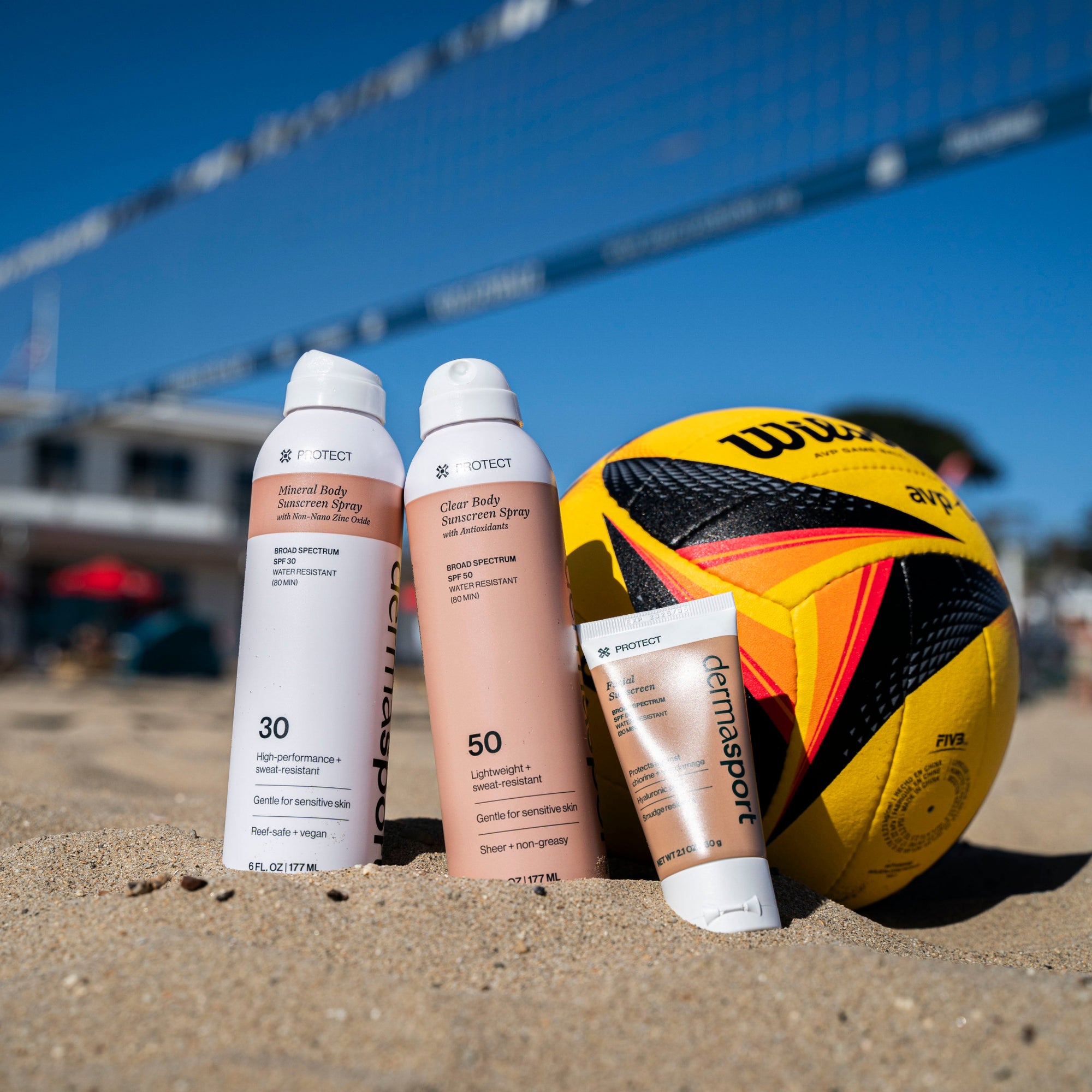 Dermasport sunscreen bottles and a volleyball on a sandy beach with a volleyball net in the background.